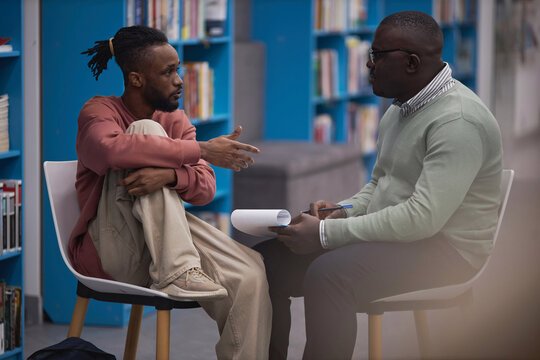 Two men talking together in a library.